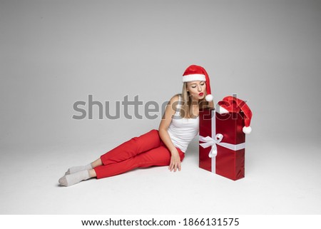 funny woman with christmas hat sits with a big red box and think what is inside, picture isolated on white background
