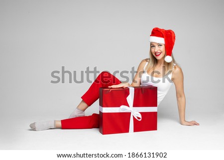 funny woman with christmas hat sits with a big red box and doesnt like it, picture isolated on white background