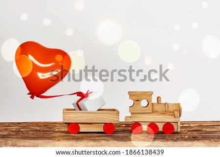 Wooden toy train hauling gift box and heart ballon on bokeh background. Happy Valentine's Day greating card. Copy space.