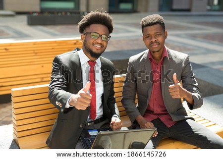 team of beautiful african people on bench with laptop in summer with hand gesture