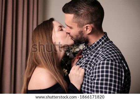 A young woman and a man are kissing while in the room. Christmas and new year celebrations.