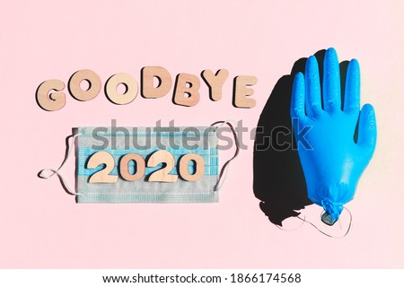 Words GOODBYE 2020 from wooden letters, inflated medical glove waving bye-bye and facemask on a pink background. Year 2020 and epidemic concept. Royalty-Free Stock Photo #1866174568
