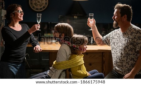 Stock photo of happy parents celebrating while their kids are gagged in a chair.