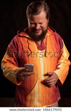 Joyful bearded man in bright orange shirt using mobile,