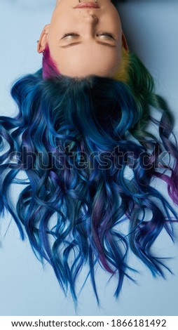 Girl with creative blue coloring and a rainbow in her hair on a blue background. Modern minimalistic bright photography for advertising and social networks