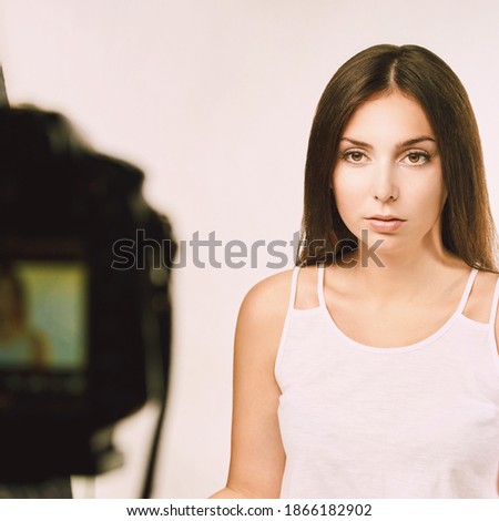 Young woman sitting near photo camera. Video blogger. Caucasian female teacher. Online education concept. Studio shoot. Light background. Record course entrepreneur. Serious face. 