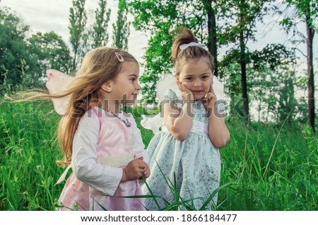 Little cute girls with butterfly wings among tall green grass in backlight with sun glare. Selective focus. Blurred background.