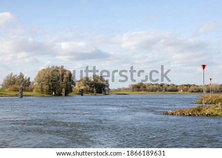 Meandering river IJssel in Zutphen, The Netherlands, in autumn landscape with fall colors in the trees in the background and signage along the river bed Royalty-Free Stock Photo #1866189631