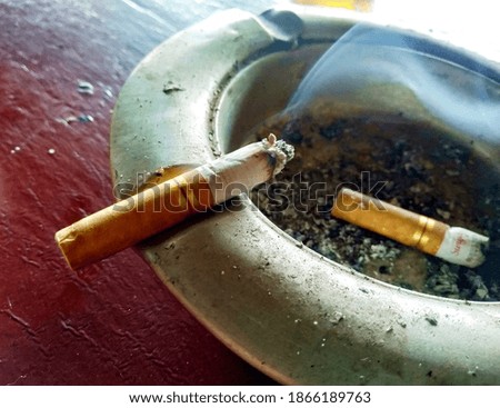 a picture of a cigarette on an ashtray that still emits dirty-looking smoke.