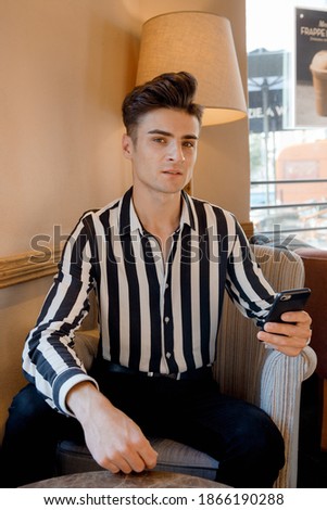 Caucasian man. Young Italian in a cafe at a table with his mobile phone. Stylish man in a coffee shop.