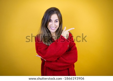 Young beautiful woman wearing red sweater over isolated yellow background smiling and pointing with hand and finger to the side