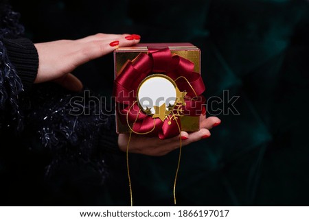 In woman hand is present, showing beautiful red gift box with copy space, closeup photo on dark background. Christmas.