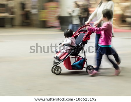 Mother with children walking in urban commercial street, blurred motion background