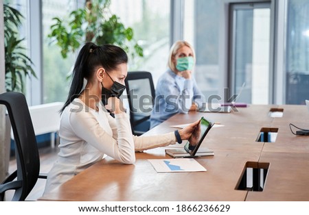 Group of employees wearing a mask sitting at a meeting and working with the tablet while introducing new normal work. Stock photo