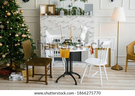 Classic interior of the vintage dining room with a marble fireplace, round table and various chairs near the Christmas tree