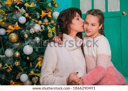 Mom and daughter are sitting on the steps at the Christmas door and waiting for the New Year. Loving family, the girl kisses the parent.
