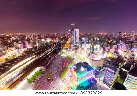 Aerial view above Taichung Railway Station in Taiwan, with the historic architecture of the old station preserved in situ, high-rise towers standing under twilight sky and city lights dazzling at dusk