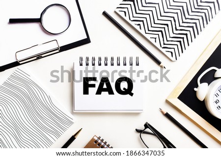 On a light table are notebooks, a magnifying glass, an alarm clock, glasses, and a pen. And in the center is a notebook with the text FAQ Frequently Asked Questions