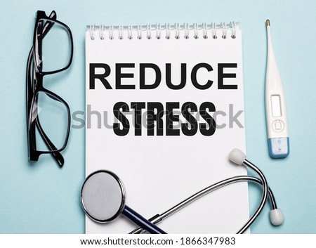 REDUCE STRESS written on a white notepad next to a stethoscope, goggles, and an electronic thermometer on a light blue background. Medical concept.