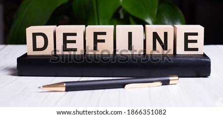 The word DEFINE is written on the wooden cubes that lie on the diary near the pen.
