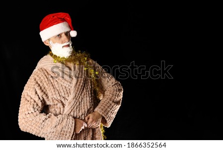 Bad Santa with a beard of shaving foam in a housecoat on a black background