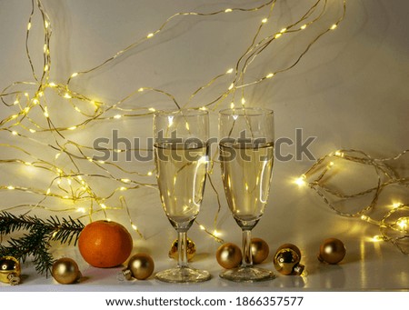 two glasses of champagne, golden glass balls and various Christmas decorations, illuminated background of a chain of white lights, waiting time for Christmas, winter