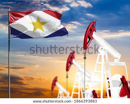 Oil rigs against the backdrop of the colorful sky and a flagpole with the flag of Saba. The concept of oil production, minerals, development of new deposits.