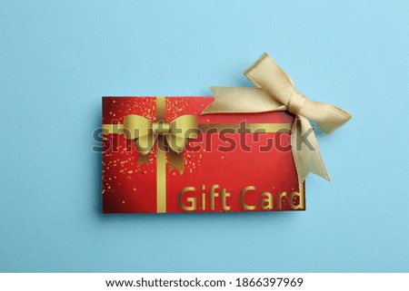 Gift card with bow on light blue background, top view