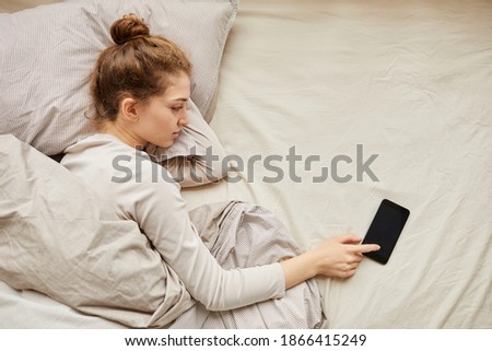 Young woman turning off her mobile phone while lying in her bed in the morning