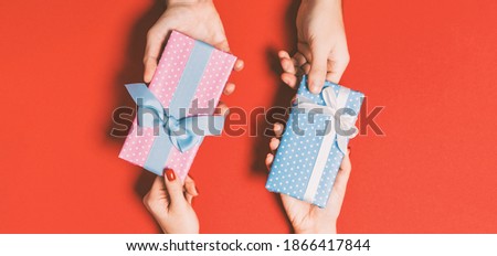 Top view of a woman and a man exchanging gifts on colorful background. Couple give presents to each other. Close up of making surprise for holiday concept.