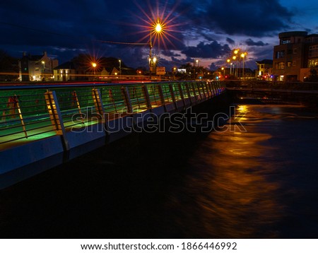 Night shot of Wolfe Tone Bridge in Galway city, Ireland, Blue sky, warm orange lights reflects in river Corrib. Pronounced lens star-burst.