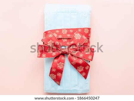 medical protective face masks as a gift with a red ribbon on a pink background. Christmas and New Year 2021 decor. Holidays self-isolation and coronavirus pandemic concept