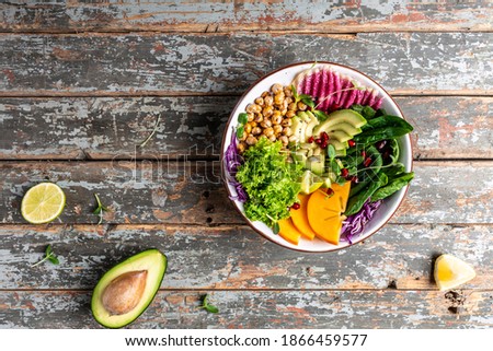 Healthy balanced eating. vegan, detox Buddha bowl dish with roasted chickpeas, avocado, persimmon, spinach, avocado, watermelon radish and seeds.