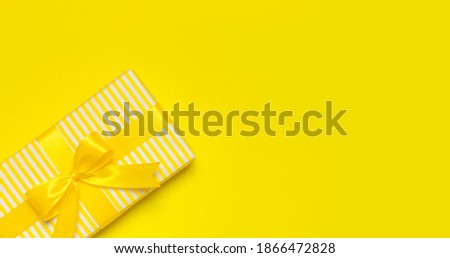Flat lay holiday background. Bright yellow gift present box with ribbon and bow on yellow background top view copy space. Birthday present, March 8, Mother's Day, Valentine's Day. Congratulation