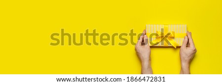 Male hands holding bright yellow gift present box with ribbon on yellow background top view. Flat lay holiday background. Birthday present, March 8, Mother's Day Valentine's Day. Congratulation Banner