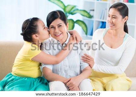 Portrait of cute little girl embracing and kissing her grandmother with young woman near by