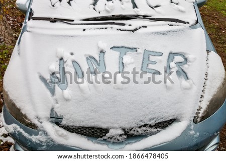 The inscription Winter, on the surface of the car hood, covered with snow