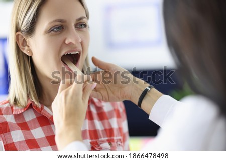Doctor looking at throat of woman patient with wooden spatula in clinic. Pharyngitis and laryngitis treatment concept Royalty-Free Stock Photo #1866478498