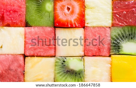 Background texture of diced tropical summer fruit cut in cubes and arranged in rows for a seamless pattern with watermelon, strawberry, kiwifruit, pineapple and melon