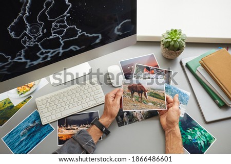 Close-up of designer looking at photos sitting at his workplace in front of computer monitor at office