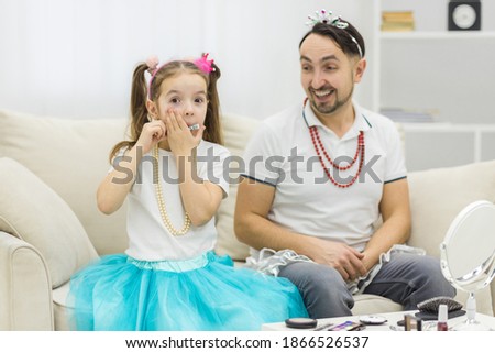 Cute little daughter and her handsome young dad in crowns are playing together.