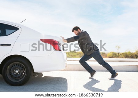 Tired man in his 30s trying hard to push his dead car to move it to the side of the road  Royalty-Free Stock Photo #1866530719