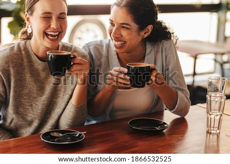Happy woman friends in a cafe having coffee. Two females sitting at a coffee table talking and laughing. Royalty-Free Stock Photo #1866532525
