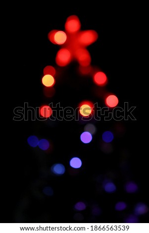 Unfocused festive Christmas background. Christmas tree silhouette with light bulbs effect and red star on top, blurred and illuminating