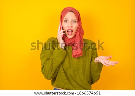 Young beautiful muslim woman wearing hijab against yellow background talking on the phone stressed with hand on face, shocked with shame and surprise face, angry and frustrated. Fear and upset for mis