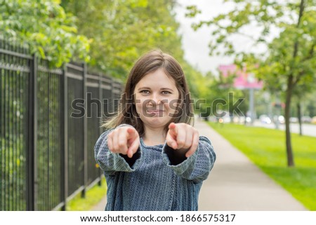 Smiling girl shows a finger forward while standing on the street against the background of the road and park. The concept is a call to move forward or we need you.