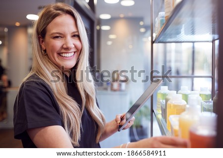 Portrait Of Female Business Owner In Hairdressing Salon With Digital Tablet Checking Beauty Products