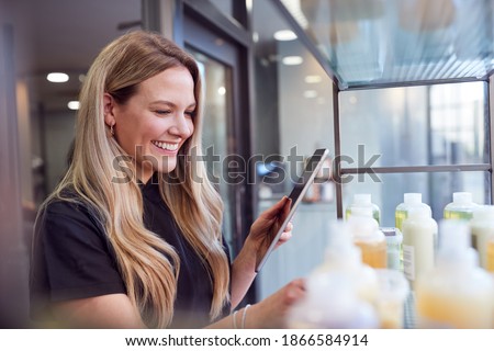 Female Stylist Or Business Owner In Hairdressing Salon Using Digital Tablet To Check Beauty Products