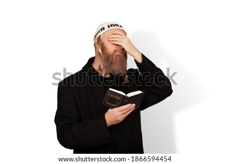 Religious Jewish man holding Siddur in his hand covering eyes with hand isolated on white background. Bearded Jew hasid with sidelocks in white kippah reads prayer. Reading Kriyat Shema Royalty-Free Stock Photo #1866594454