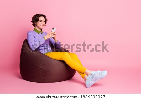 Full body profile side photo of positive girl sit bean chair use smartphone wear pants isolated pastel color background